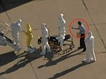 As coverage of the transport of the Dallas second health care worker diagnosed with Ebola aired live on NBC 5, viewers questioned a sight at Love Field Wednesday: A man in plain clothes standing among those in hazmat suits.While three people helped Amber Vinson out of an ambulance, off a stretcher and up the stairs to a specially equipped jet taking her to Atlanta for treatment at Emory University Hospital, a man wearing no protective gear stood nearby holding a yellow envelope.